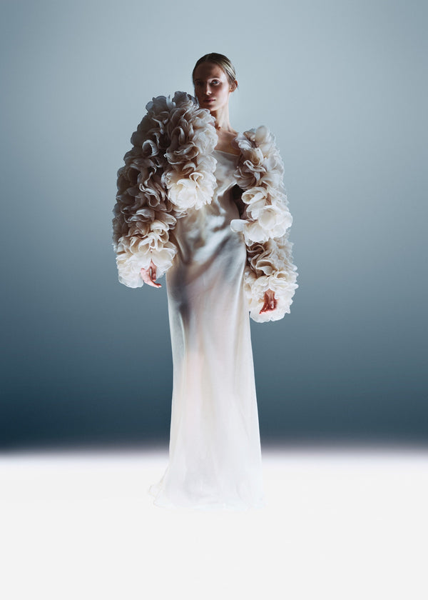 Woman wearing a white wedding dress with floral embellishments against a gray background
