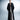 Person wearing a long black coat over a white outfit on a gray background