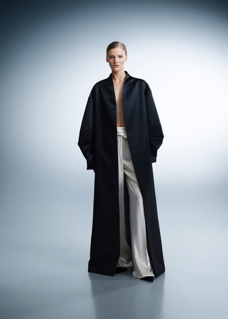 Person wearing a long black coat over a white outfit on a gray background